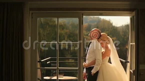在阳台上温柔地拥抱美丽的新娘和英俊的新郎蜜月概念视频的预览图