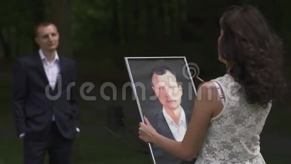 美丽的深色头发的年轻女艺术家在森林的户外画她丈夫的画像视频的预览图