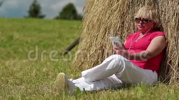 有着白色智能手机的女人坐在干草堆旁听音乐视频的预览图