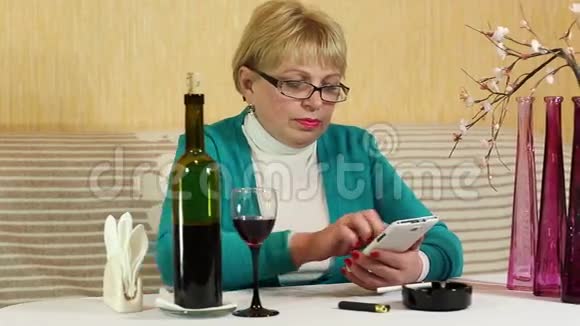 女人坐在桌边喝红酒用智能手机视频的预览图