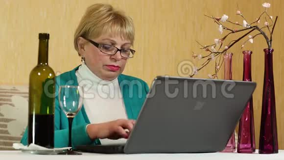 有一瓶酒的女人坐在桌子旁在笔记本电脑上输入文字视频的预览图