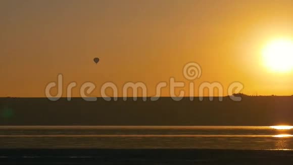 在绚丽的金色和橙色的日落中气球飞过海岸视频的预览图