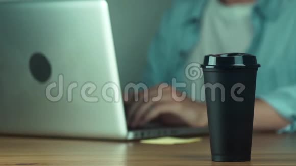 年轻人用笔记本电脑打字男人拿着黑色的热杯视频的预览图