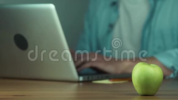 年轻人用笔记本电脑打字从桌子上拿出一个绿色的苹果视频的预览图