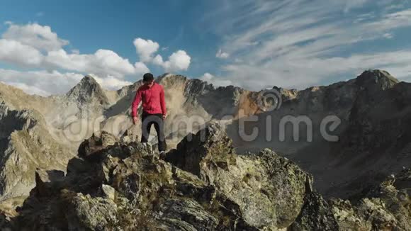 一个留着胡子的年轻人一个戴着帽子和太阳镜的登山者爬上了高山上的一个岩石岭公园游视频的预览图