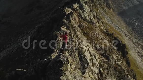 一个留着胡子的年轻人一个戴着帽子和太阳镜的登山者爬上了高山上的一个岩石岭公园游视频的预览图