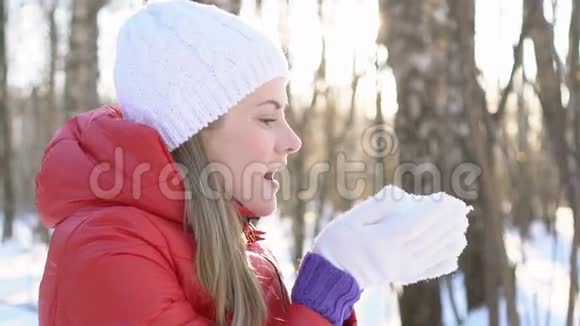 美丽的年轻女子在冬天的公园里吹雪玩得很开心微笑着慢动作视频的预览图
