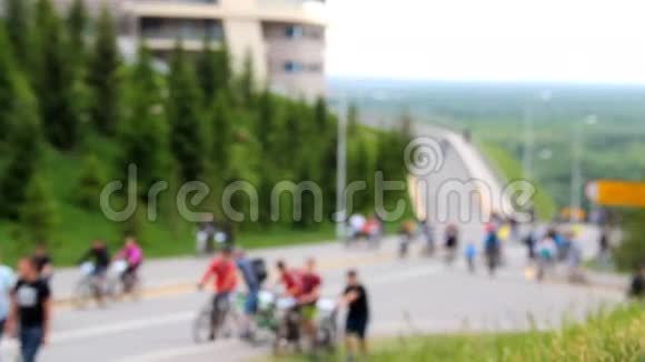 许多骑自行车的人和步行者沿着公路走山上长满了绿草和毛皮树视频的预览图