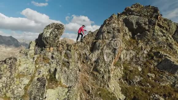 一个留着胡子的年轻人一个戴着帽子和太阳镜的登山者爬上了高山上的一个岩石岭公园游视频的预览图