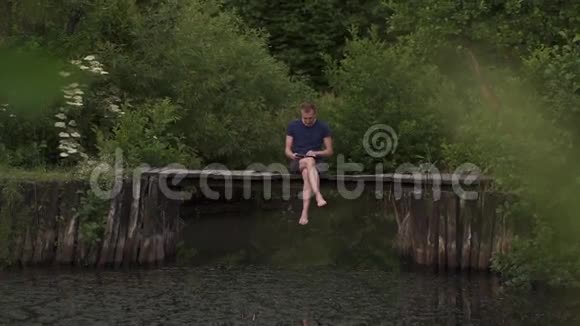 在夏天男人坐在河上的一个木制浮舟上在妻子去世时使用数字平板电脑视频的预览图