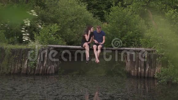 夏天一对夫妇坐在河边的一个木桥上丈夫用数码平板电脑妻子想画他的视频的预览图