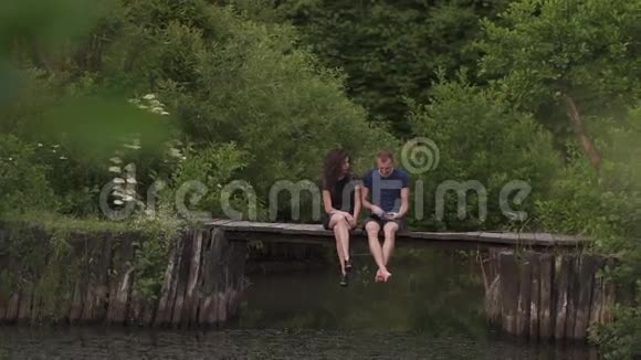 夏天一对迷人的优雅夫妇坐在河边的一个木制浮舟上使用一台数字平板电脑视频的预览图