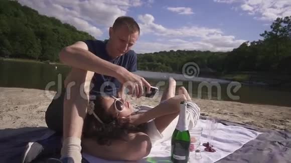 在炎热的夏日在沙滩上两个露露在野餐上用葡萄酒和糖果放松直到男人开始发短信为止视频的预览图
