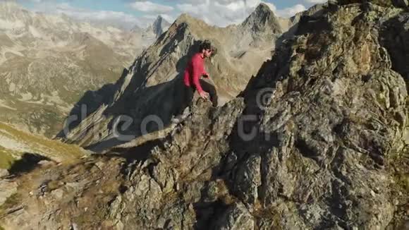 一个留着胡子的年轻人一个戴着帽子和太阳镜的登山者爬上了高山上的一个岩石岭公园游视频的预览图