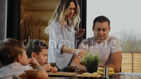 一家四口在他的厨房里吃早餐窗户很大人们微笑着母亲亲吻拥抱视频的预览图