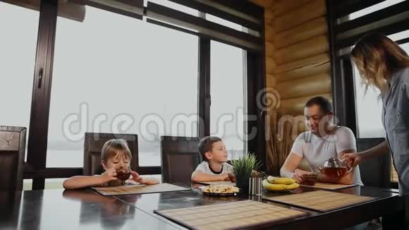 一家四口在他的厨房里吃早餐窗户很大人们微笑着母亲亲吻拥抱视频的预览图