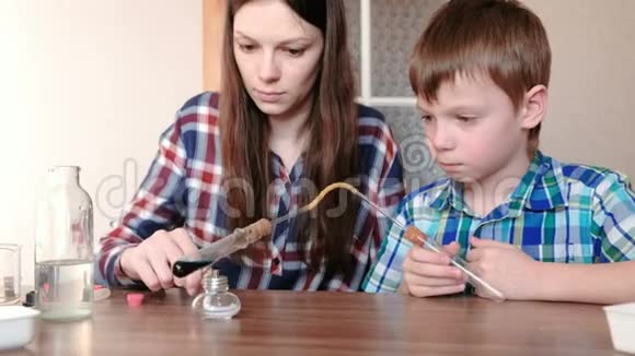 家庭化学实验男孩和他妈妈在燃烧的酒精灯上用蓝色液体加热试管视频的预览图