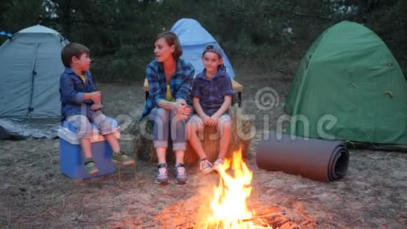 家庭周末在森林妈妈和孩子在篝火旁交流年轻的家庭在背景帐篷和树木视频的预览图