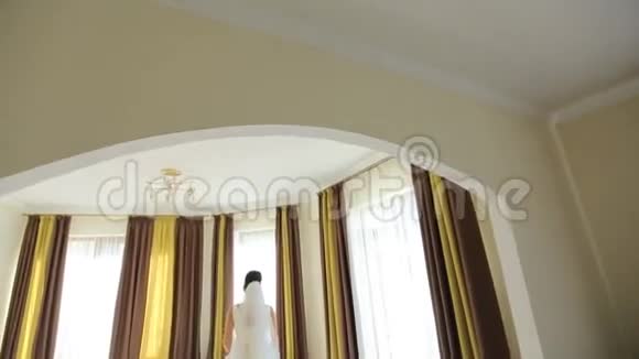 美丽的新娘穿着华丽的白色连衣裙走向窗户视频的预览图