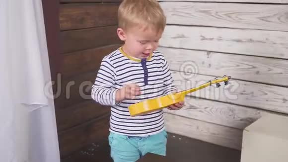 一岁的男孩弹吉他或四弦琴唱歌坐在木房里视频的预览图