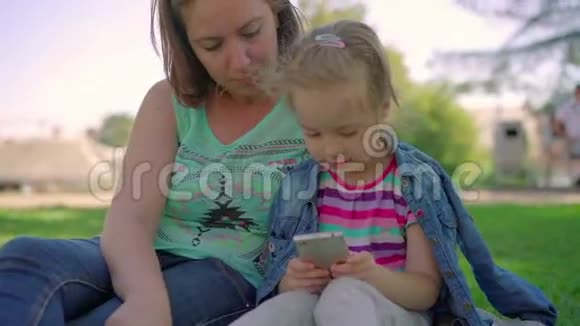妈妈和女儿在公园里打电话玩游戏视频的预览图