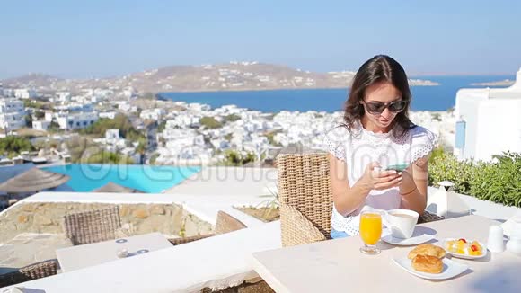 美丽优雅的女士早餐与电话在户外咖啡馆令人惊叹的景观Mykonos镇视频的预览图