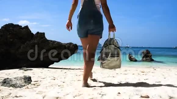 年轻的女孩一头漂亮的头发穿着工作服背着背包在美丽的白色海滩上带着岩石视频的预览图