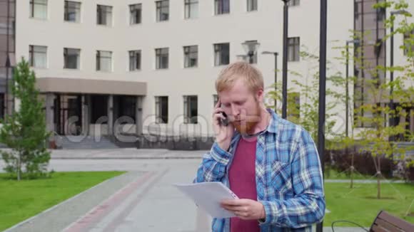 一个年轻的学生来到大学的背景下打电话拿着重要的文件视频的预览图