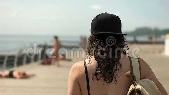 戴着棒球帽的女孩背着背包在河堤上行走视频的预览图