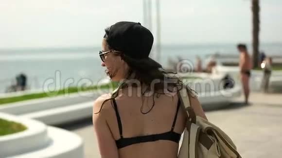 戴着棒球帽的女孩背着背包在河堤上行走视频的预览图