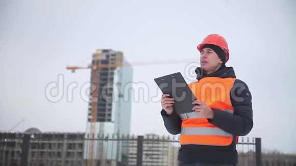 建筑设计师戴着头盔和橙色背心的工人在多层房屋起重机的背景下过冬视频的预览图