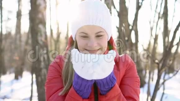 美丽的年轻女子在冬天的公园里吹雪玩得很开心微笑着慢动作视频的预览图