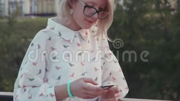 年轻的美女在湖边的城市公园里用智能手机发短信给朋友上网视频的预览图