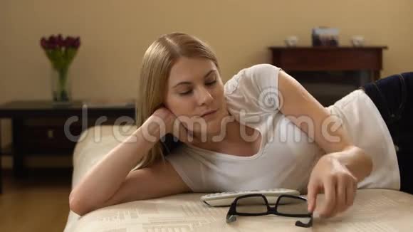漂亮的年轻女人躺在沙发上在智能电视上安装3d眼镜开关观看3d电影视频的预览图