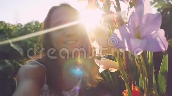 年轻美丽浪漫的女人在户外的花朵日落时通过太阳缓慢地运动有强烈的耀斑效应视频的预览图