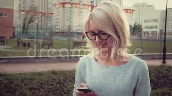 快乐的年轻女子站在公园里的人群中使用她的智能手机发短信视频的预览图