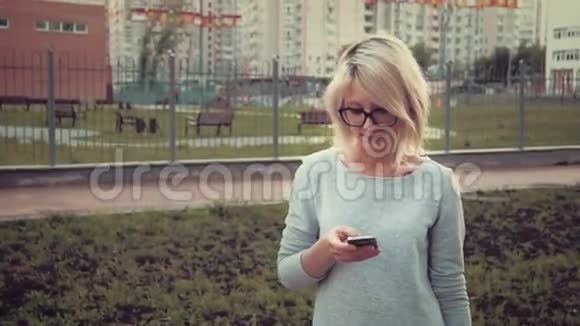 快乐的年轻女子站在公园里的人群中使用她的智能手机发短信视频的预览图