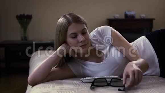 年轻漂亮的女人躺在沙发上在智能电视上安装3d眼镜开关观看3d电影视频的预览图