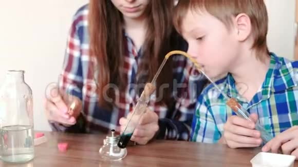 家庭化学实验男孩和他妈妈在燃烧的酒精灯上用蓝色液体加热试管视频的预览图