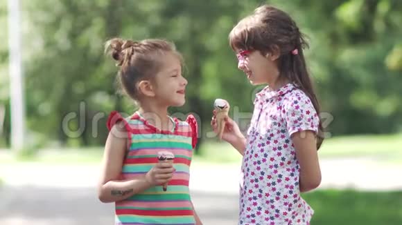 无忧无虑的孩子在夏天公园吃冰淇淋两个小女孩开心地交谈和微笑视频的预览图