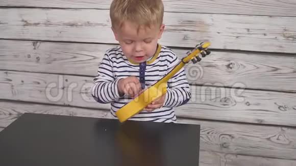 快乐的一岁男孩弹吉他或四弦琴唱歌坐在木房里视频的预览图