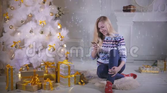 漂亮的女孩使用手机在圣诞夜坐在圣诞树附近视频的预览图