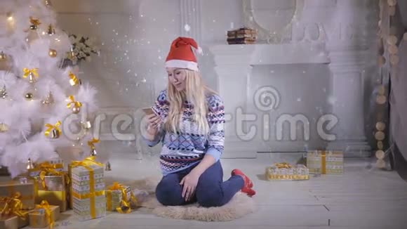 漂亮的女孩使用手机在圣诞夜坐在圣诞树附近视频的预览图