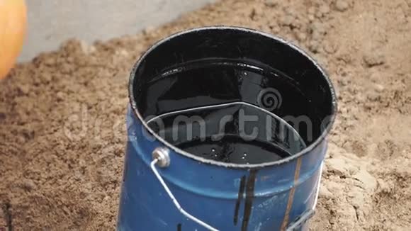 滚浸在蓝色桶中在砂面上涂上黑色焦油或油漆视频的预览图