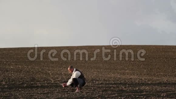 一个留胡子的人带着手机在田野里的肖像一个人光着脚在田野里给植物拍照视频的预览图