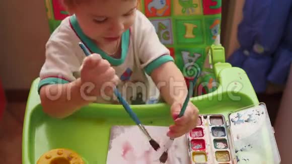 一个快乐的孩子用画笔在纸上画画视频的预览图