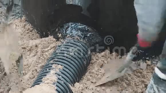 两名工人用铲子和靴子在黑色塑料管周围压缩沙子视频的预览图