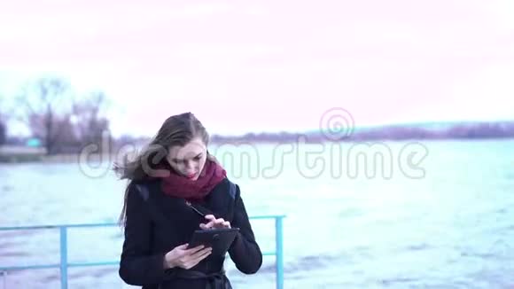 年轻漂亮的女人在湖边用平板电脑4k视频的预览图
