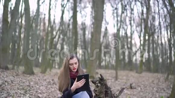 漂亮的女孩坐在树桩上用平板电脑4k视频的预览图