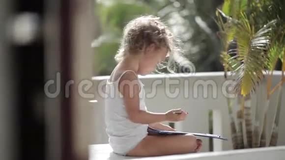 女孩用铅笔在阳台的纸上画背景是棕榈树视频的预览图